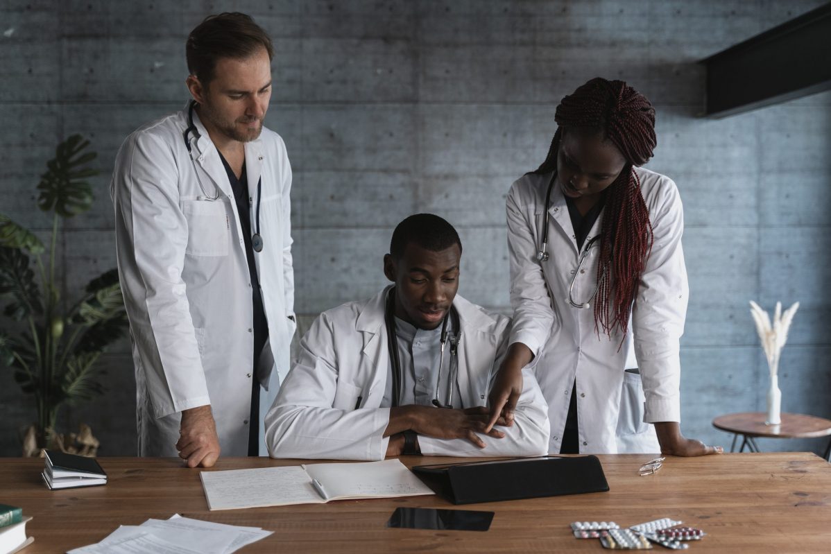 Three physicians in front of a table reviewing notes.