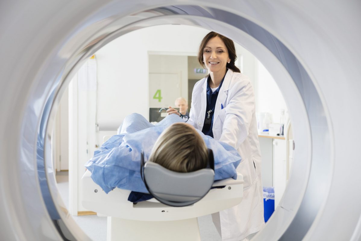 Patient on a stretcher entering a CT scan machine while being reassured by a nurse.