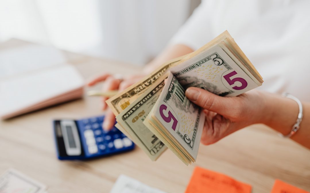 person holding american currenct while typing into a calculator